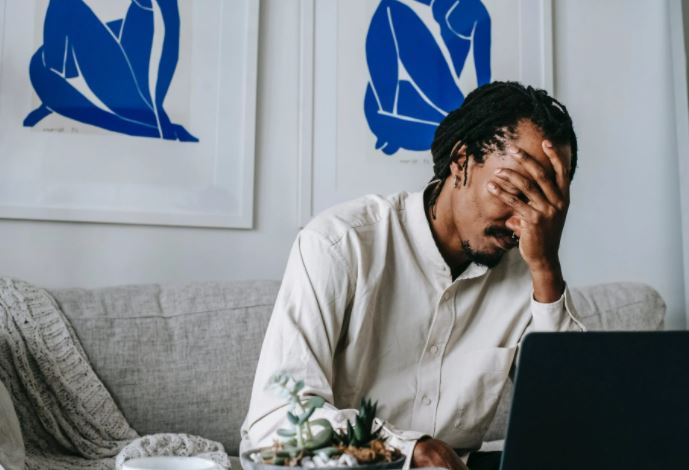 Man covering his face while working on his laptop from home.